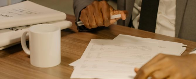 Free Close-up of a businessman holding and reviewing documents on a wooden desk. Stock Photo
